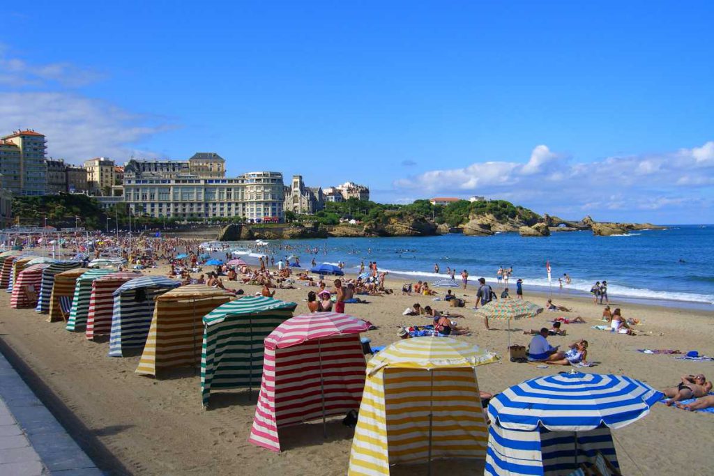 Ein beliebter Urlaubsort am Atlantik - Jetset Flair inklusive Farbige Schirme säumen den Strand von Biarritz im Hintergrund ein riesiges Hotel.