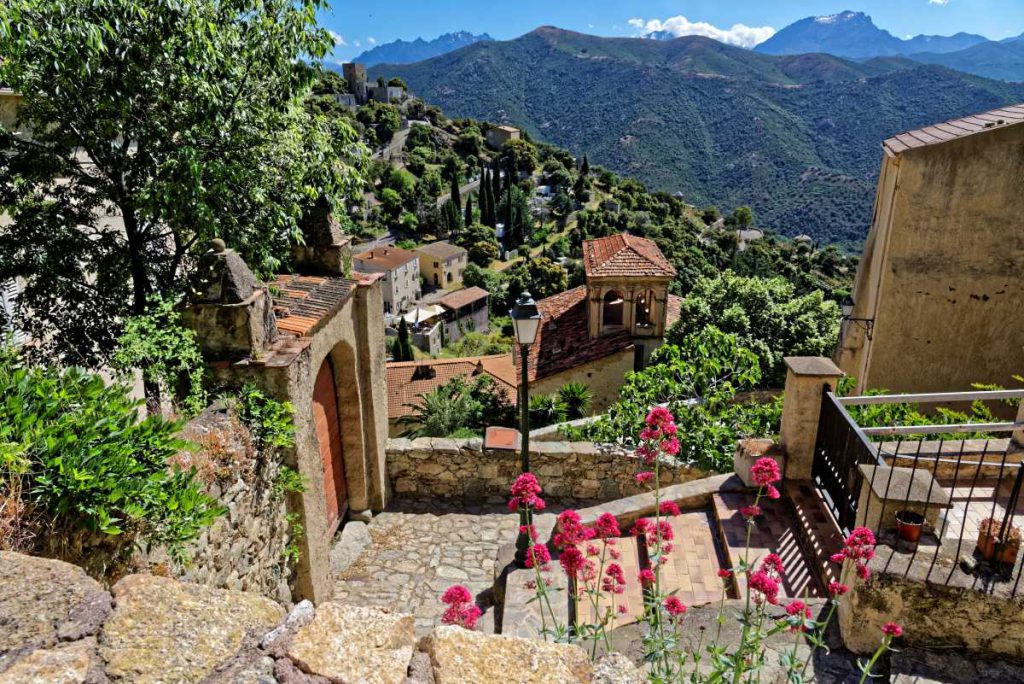 Bergidylle auf Korsika Blick auf ein kleines Bergdorf mit bergiger Kullise und alten Steintreppen, die zu antiken Sandstein-Gebäuden führen